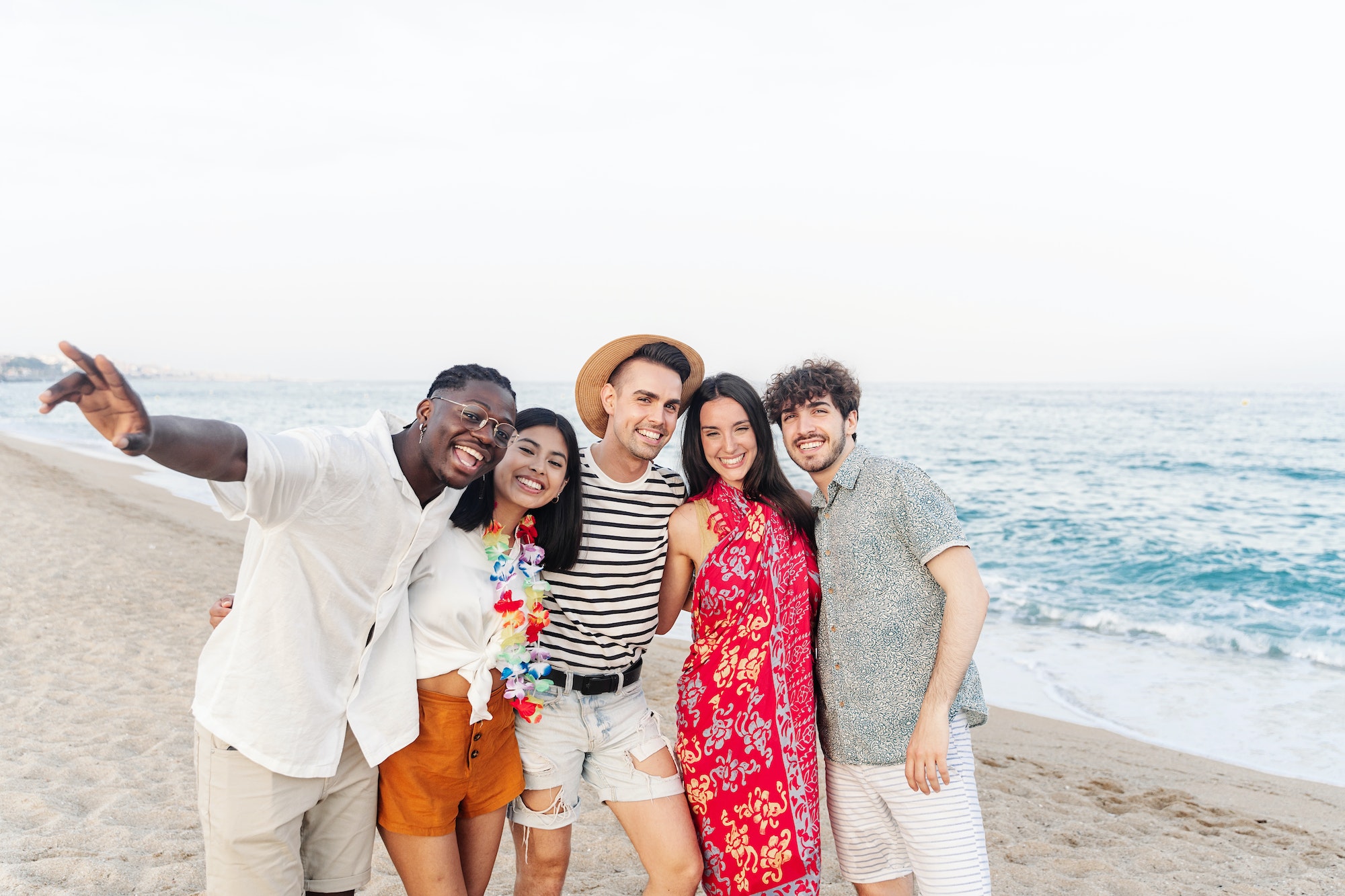 Happy multi ethnic friends hanging out having fun outdoors on the beach